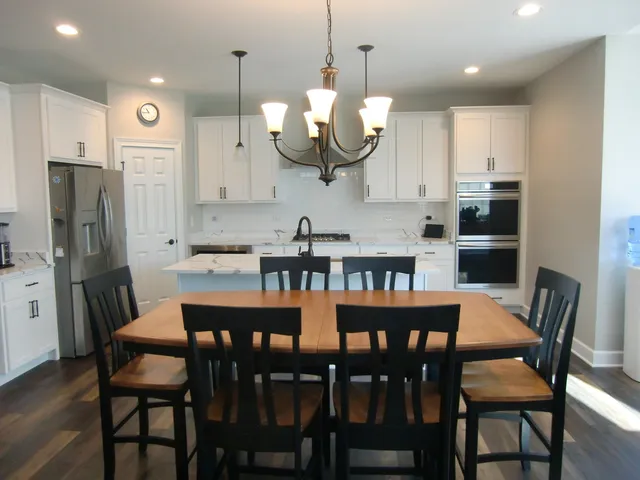 a kitchen with stainless steel appliances granite countertop a dining table chairs refrigerator and microwave