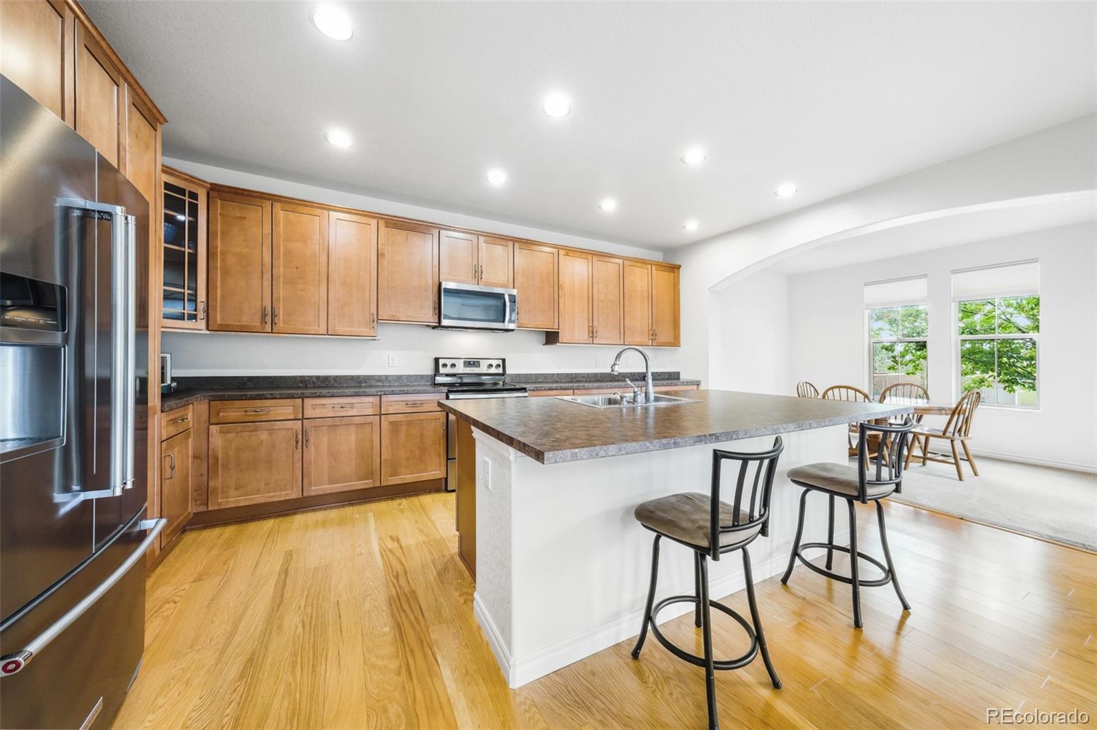 9550 Rosato Court Highlands Ranch, CO 80126 - Photo 9 of 27 a kitchen with stainless steel appliances granite countertop a refrigerator a sink dishwasher a stove and a dining table with wooden floor