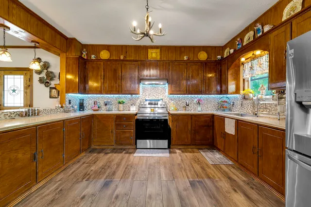a kitchen with stainless steel appliances kitchen island granite countertop a refrigerator a stove top oven a sink dishwasher and white cabinets with wooden floor