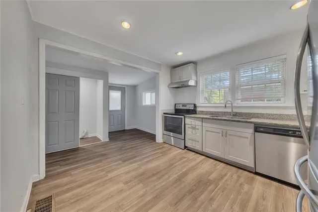a kitchen with stainless steel appliances granite countertop a stove a sink and a refrigerator with wooden floors