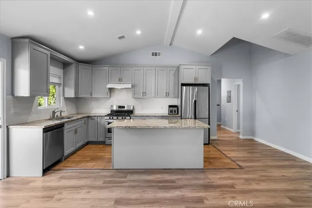 a large kitchen with stainless steel appliances granite countertop a stove a sink dishwasher and a refrigerator with wooden floor