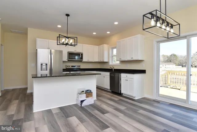 a kitchen view with stainless steel appliances a kitchen island hardwood floor sink and window