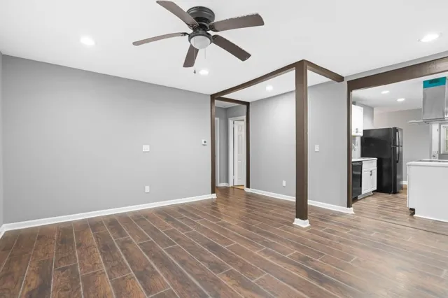 a view of an empty room and kitchen view with wooden floor