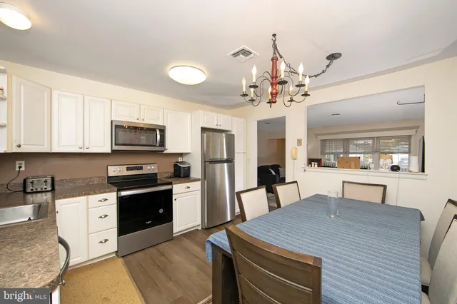 a kitchen with stainless steel appliances kitchen island granite countertop a refrigerator a stove top oven a sink dishwasher and white cabinets with wooden floor