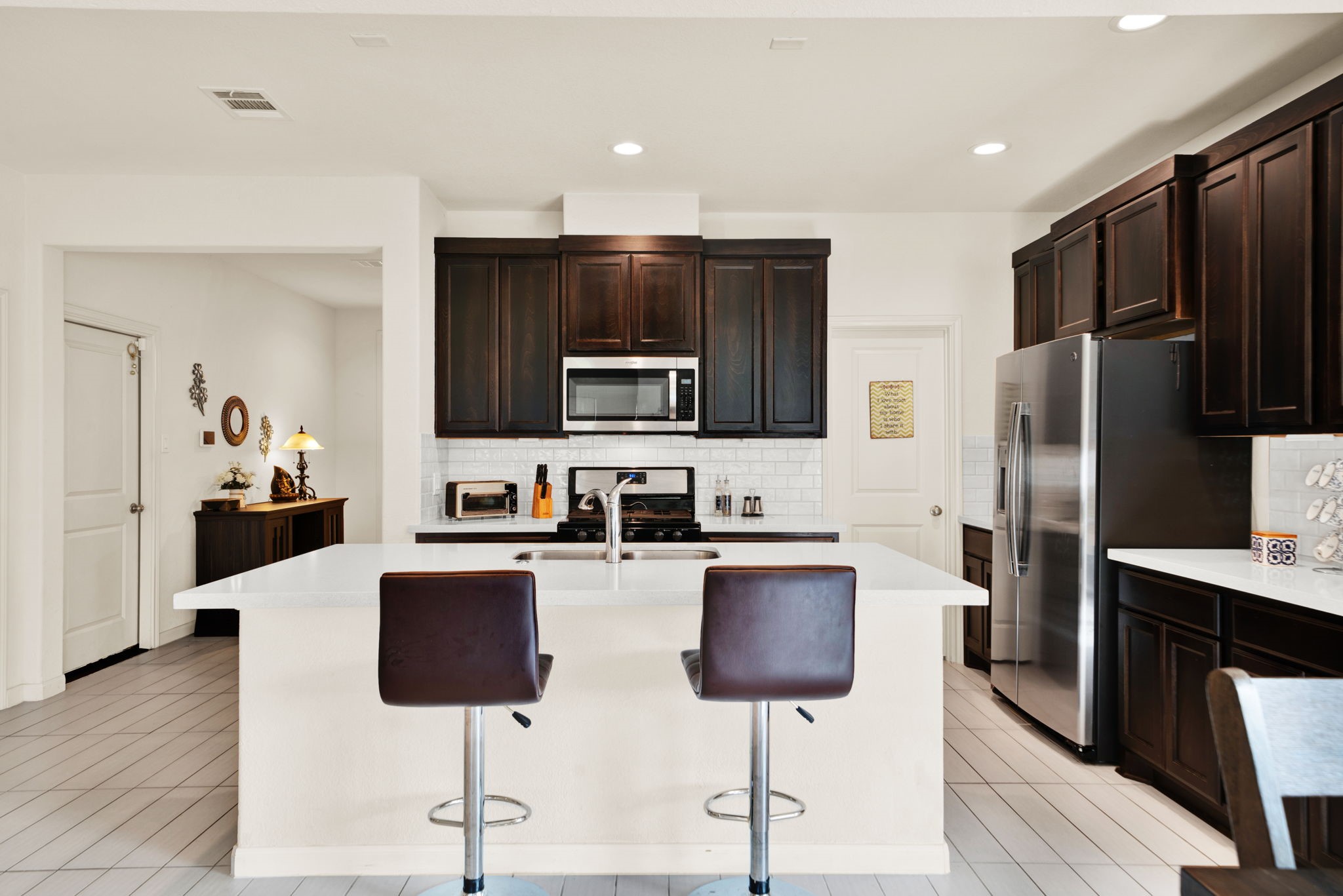 2503 Hagerman Road Conroe, TX 77384 - Photo 10 of 43 This modern kitchen features dark wood cabinetry, stainless steel appliances, and a spacious island with a sink and seating for two. The bright, open layout and tile flooring add to its contemporary feel.