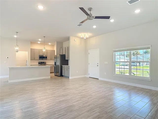 a view of an empty room with wooden floor and a kitchen