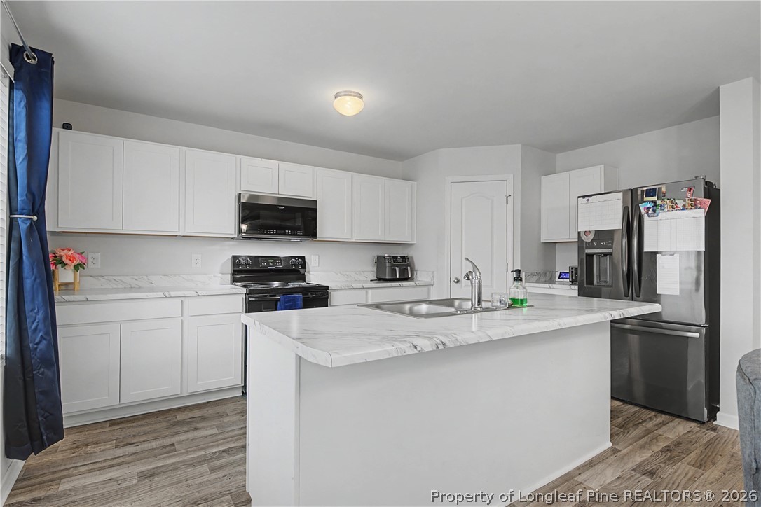 1717 Ennismore Road Hope Mills, NC 28348 - Photo 9 of 33 a kitchen with stainless steel appliances granite countertop a refrigerator stove a sink and white cabinets with wooden floor