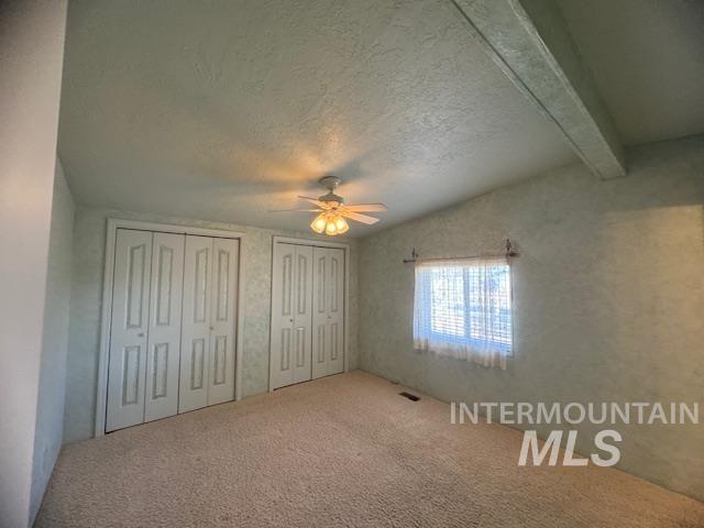 910 Moonglo, Unit 49 Buhl, ID 83316 - Photo 10 of 16 Unfurnished bedroom with multiple closets, carpet, a ceiling fan, beamed ceiling, and a textured ceiling