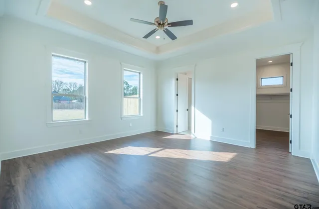 an empty room with wooden floor chandelier fan and windows