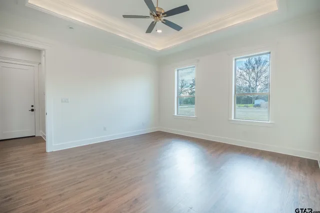 an empty room with wooden floor windows and fan