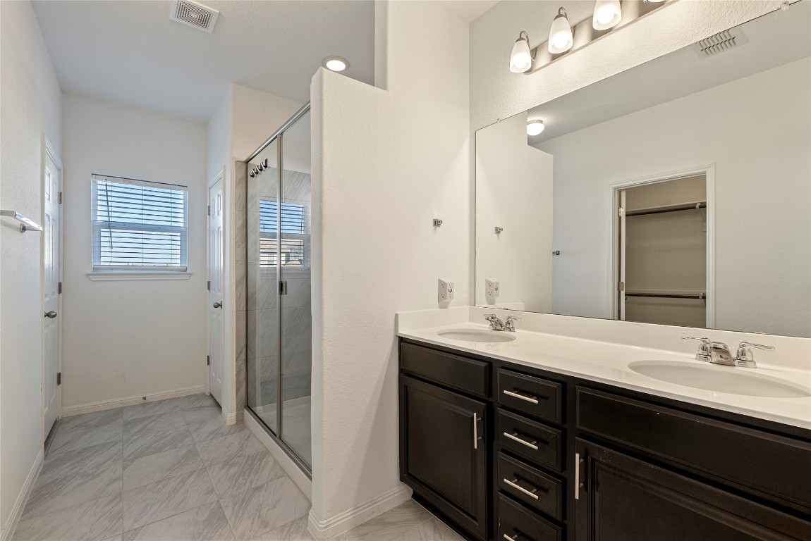 10704 Sentinel Drive Austin, TX 78747 - Photo 9 of 22 Bathroom with double vanity, a stall shower, a spacious closet, and light marble finish floors