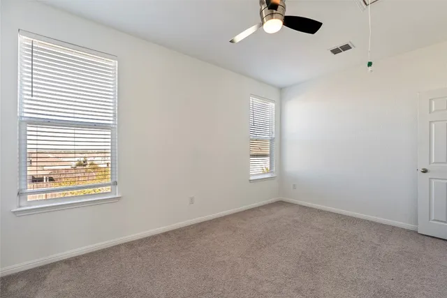 an empty room with ceiling fan and windows