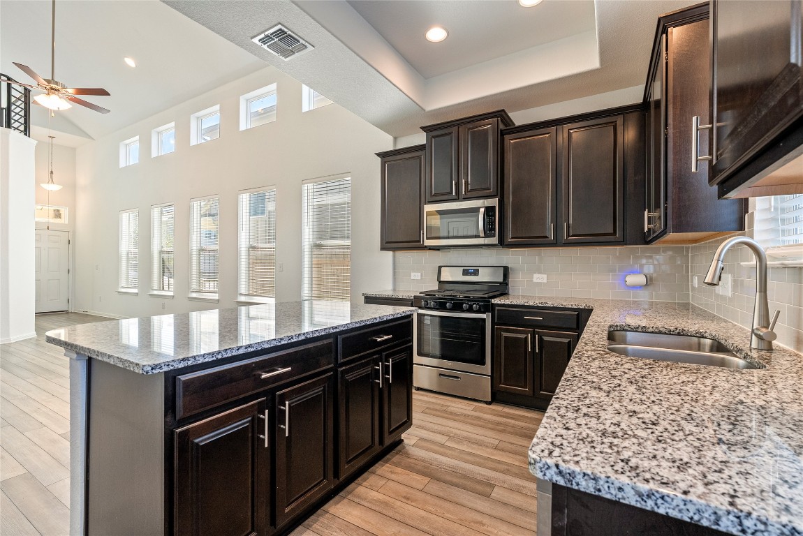 10704 Sentinel Drive Austin, TX 78747 - Photo 6 of 22 Kitchen with appliances with stainless steel finishes, backsplash, light stone counters, dark brown cabinetry, and light wood-type flooring
