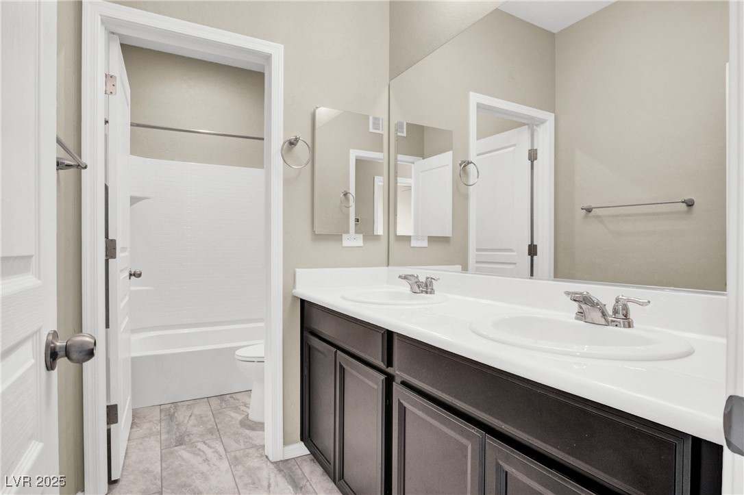 10976 Bluebell Basin Road Las Vegas, NV 89179 - Photo 29 of 40 Bathroom featuring double vanity, toilet, marble look tiles, and bathtub / shower combination