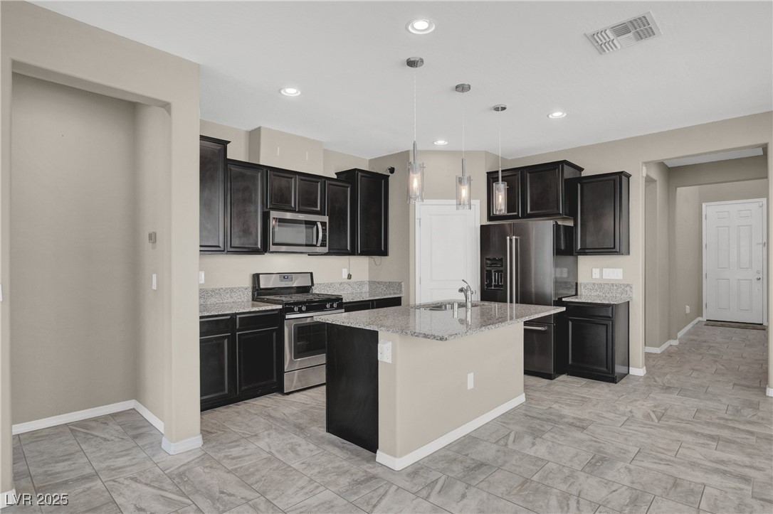 10976 Bluebell Basin Road Las Vegas, NV 89179 - Photo 7 of 40 Kitchen with appliances with stainless steel finishes, baseboards, dark cabinets, a sink, and light stone countertops