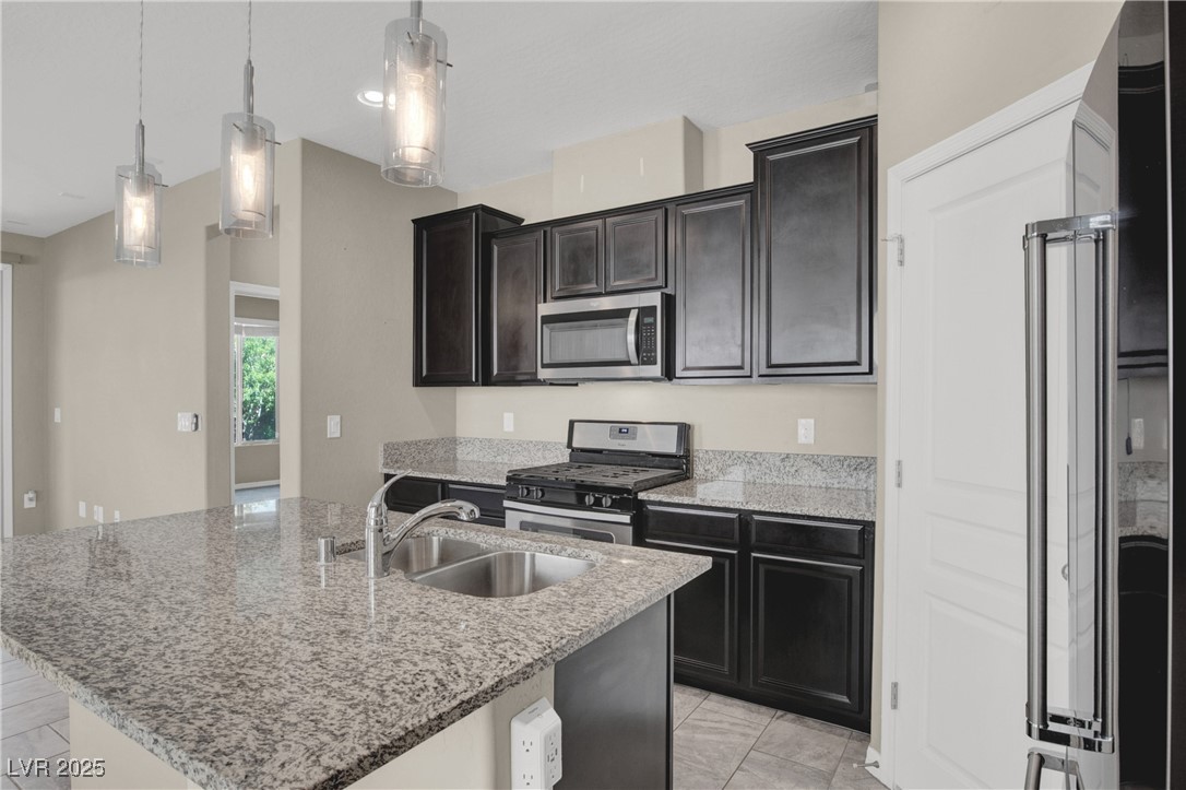 10976 Bluebell Basin Road Las Vegas, NV 89179 - Photo 8 of 40 Kitchen with stainless steel appliances, a sink, a kitchen island with sink, and light stone countertops
