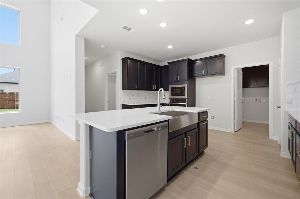 1908 Sangallo Lane Celina, TX 75009 - Photo 21 of 35 Kitchen island featuring a stainless steel farmhouse sink, integrated dishwasher, and white countertop