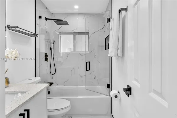 a bathroom with a granite countertop bathtub shower sink vanity and toilet