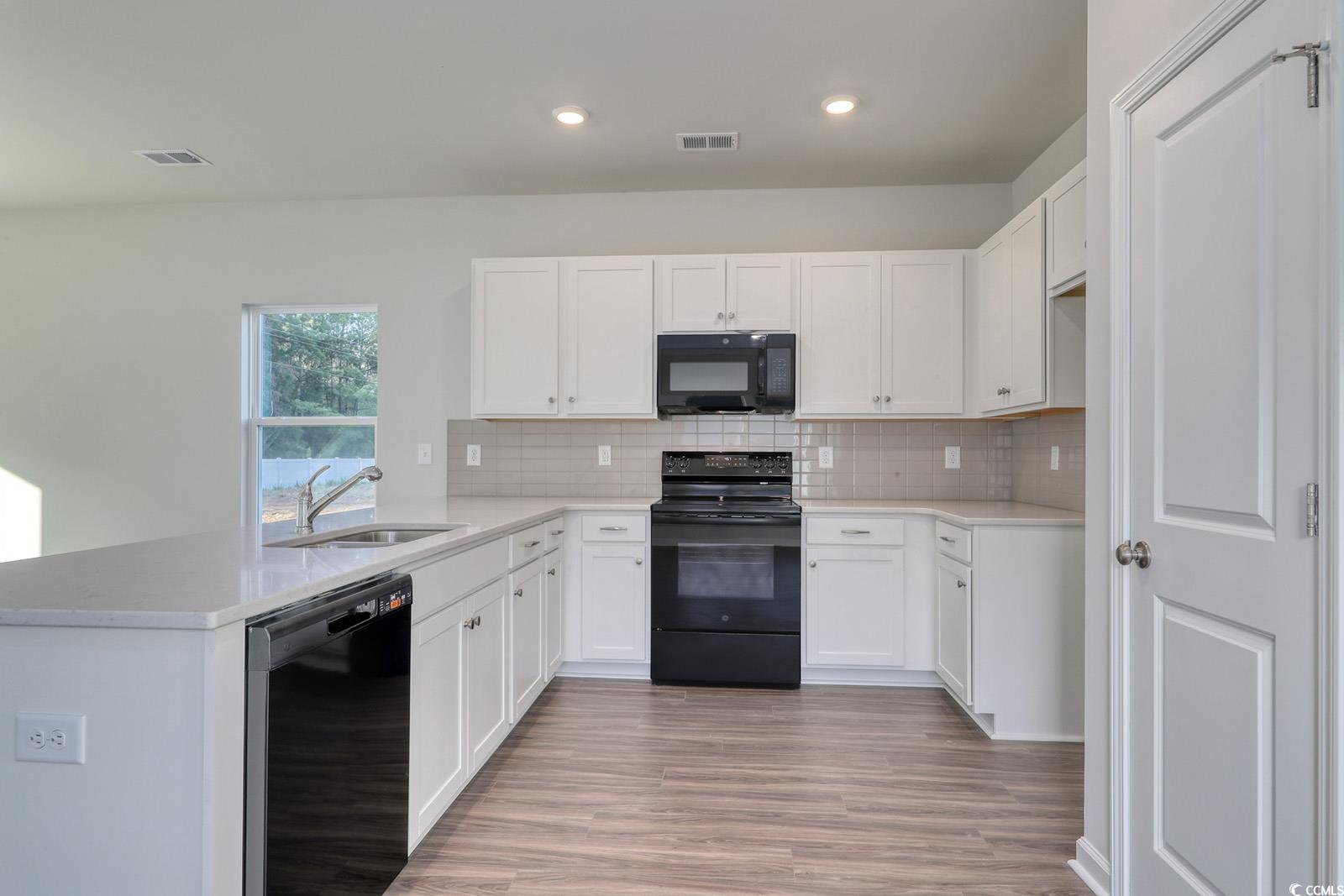 1121 Hainer Place Drive Conway, SC 29526 - Photo 3 of 28 Kitchen with black appliances, white cabinetry, a peninsula, tasteful backsplash, and light wood-style floors