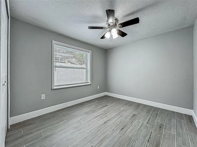 an empty room with wooden floor chandelier fan and windows