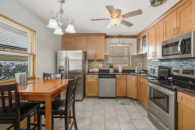 a kitchen with stainless steel appliances granite countertop a stove top oven a refrigerator a sink a dining table and chairs with wooden floor