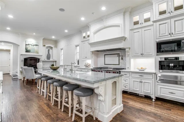 a kitchen with stainless steel appliances granite countertop a stove top oven a sink dishwasher a dining table and chairs with wooden floor