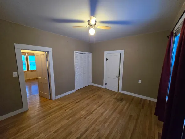 a view of an empty room with wooden floor and a ceiling fan