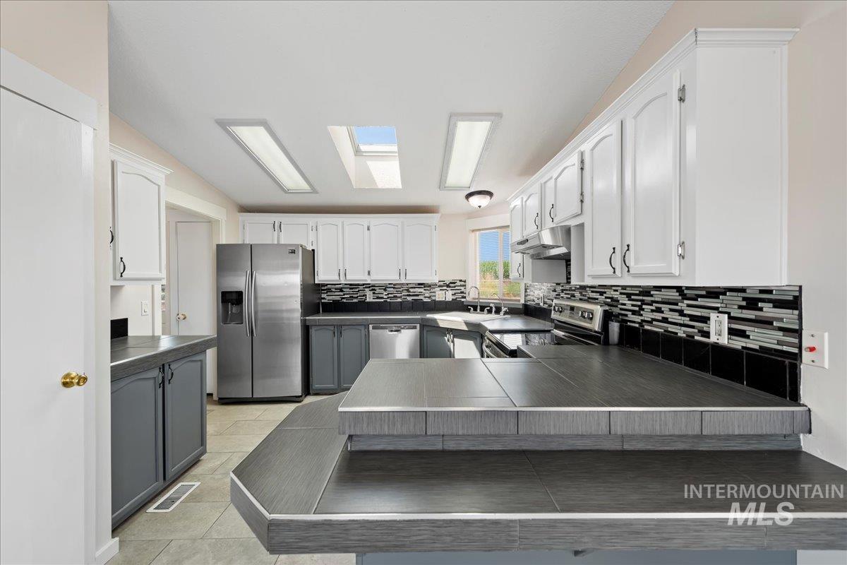 14490-14492 Sand Hollow Road Caldwell, ID 83607 - Photo 38 of 50 Kitchen with dark countertops, tasteful backsplash, white cabinetry, and stainless steel appliances
