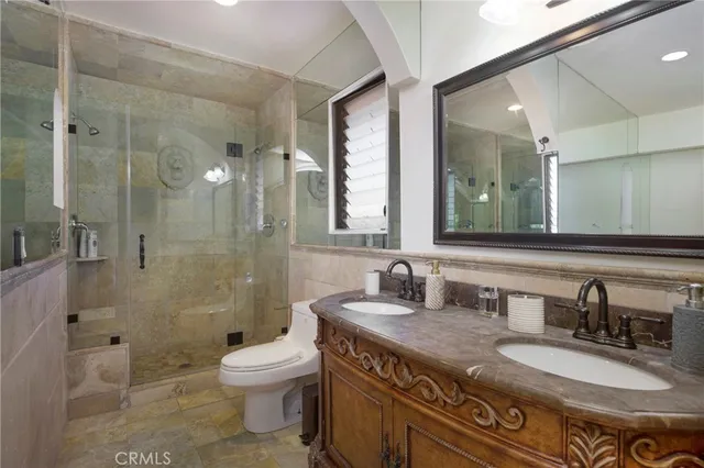 a bathroom with a granite countertop double vanity sink toilet mirror and shower