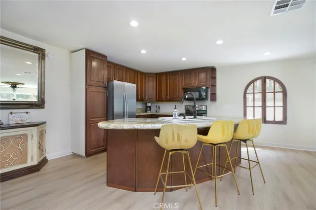 a kitchen with stainless steel appliances granite countertop a stove a refrigerator a sink a dining table and chairs with wooden floor