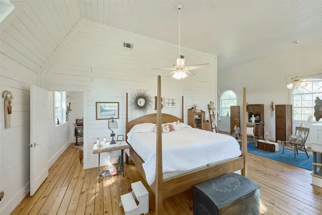 a bedroom with a bed a mirror on dresser and a wooden floor