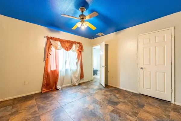 a view of an empty room with window chandelier fan and a kitchen view
