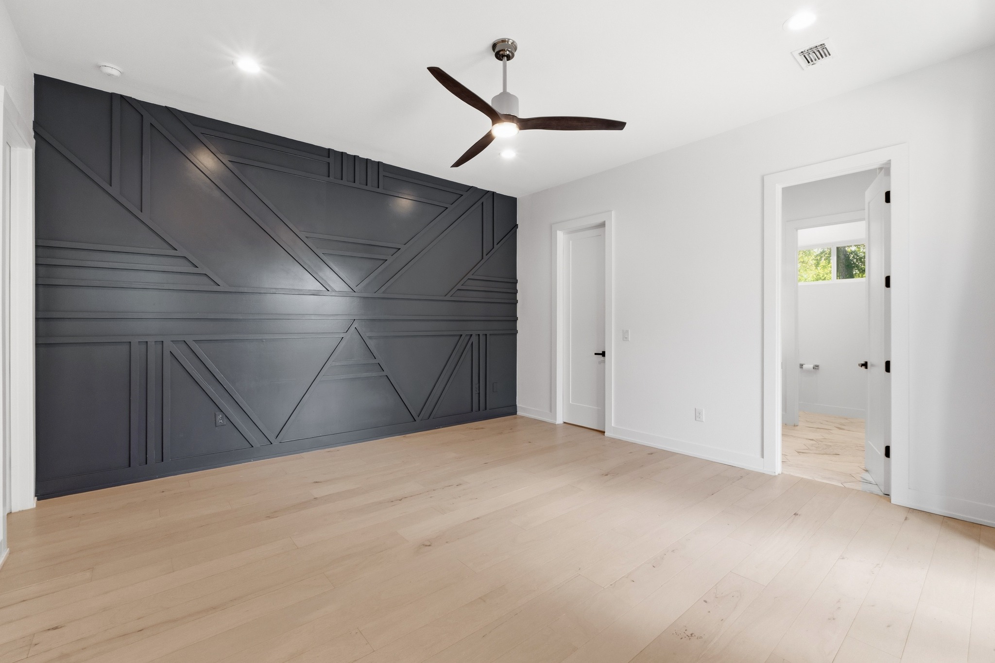 3304 East 17th Street, Unit B Austin, TX 78721 - Photo 15 of 35 A striking custom charcoal accent wall with geometric molding anchors this spacious primary room with light hardwood flooring.