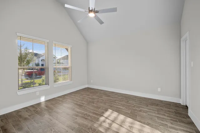 an empty room with wooden floor fan and windows