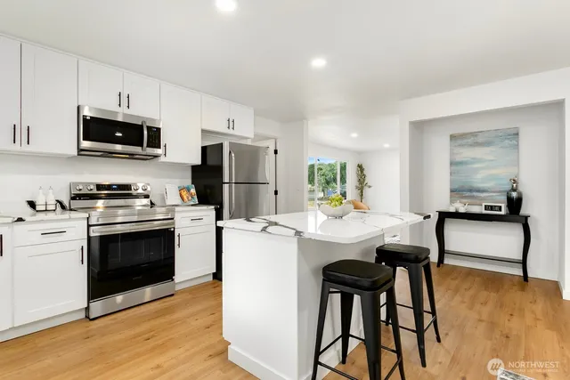 a kitchen with stainless steel appliances a stove a sink a microwave a refrigerator and white cabinets