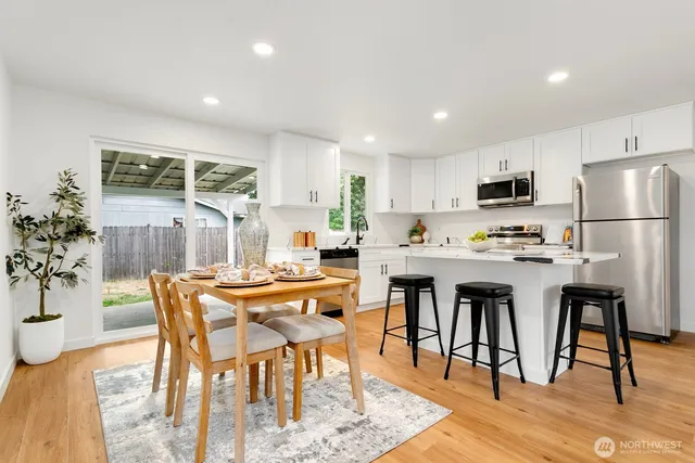 a kitchen with stainless steel appliances kitchen island granite countertop a refrigerator a stove a microwave oven a dining table and chairs with wooden floor