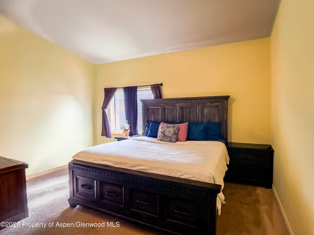 a bed sitting in a bedroom next to a window with a chair