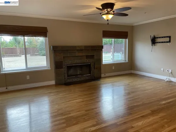 an empty room with wooden floor a chandelier fan and a fireplace