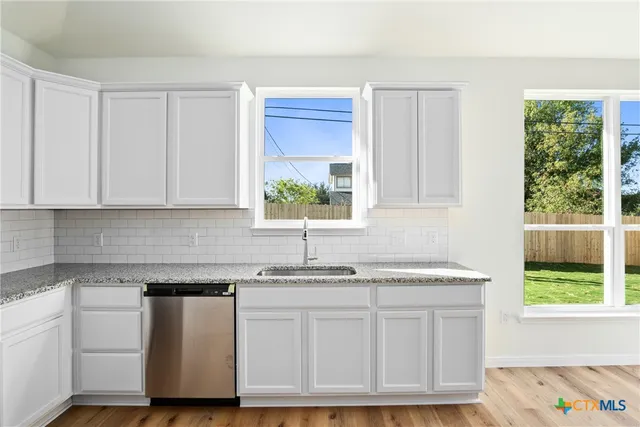 a kitchen with granite countertop white cabinets sink and stainless steel appliances