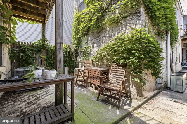 a patio with table and chairs with potted plants and large trees