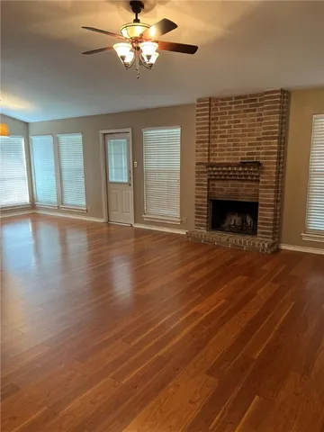 a view of an empty room with wooden floor fireplace and a window