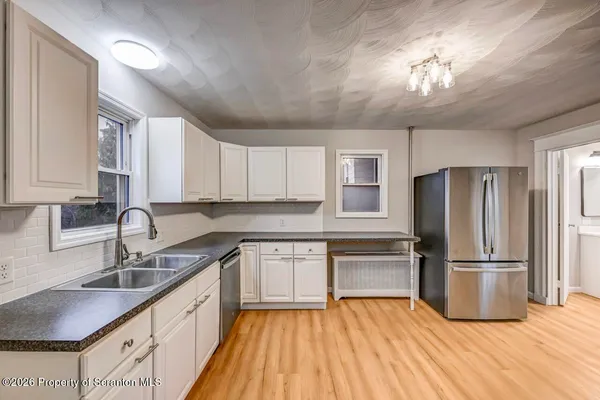 a kitchen with stainless steel appliances granite countertop a refrigerator a sink dishwasher a stove with white cabinets and wooden floor