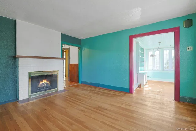 a view of an empty room with wooden floor fireplace and a window