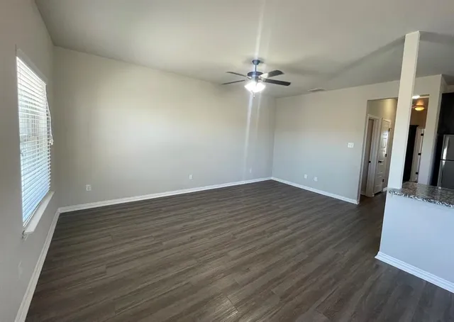 an empty room with wooden floor fan and windows