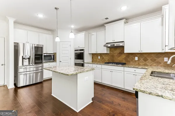 a kitchen with stainless steel appliances granite countertop a refrigerator a stove and white cabinets with wooden floor