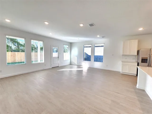 a view of an empty room with a window and kitchen view