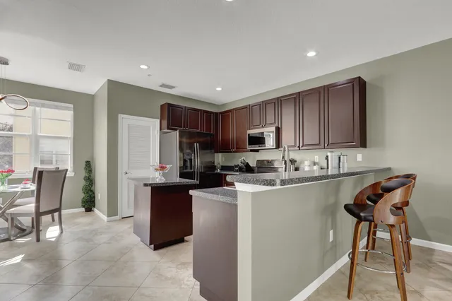 a kitchen with stainless steel appliances kitchen island granite countertop a refrigerator a stove a sink a dining table and chairs with wooden floor