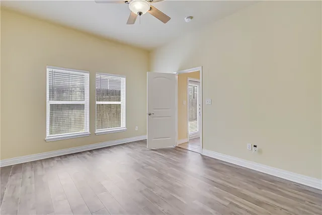 an empty room with wooden floor chandelier fan and windows