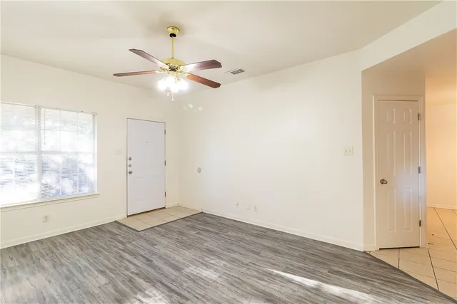 an empty room with wooden floor fan and windows