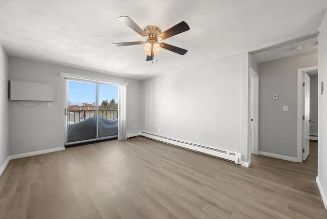 a view of an empty room with wooden floor and a ceiling fan
